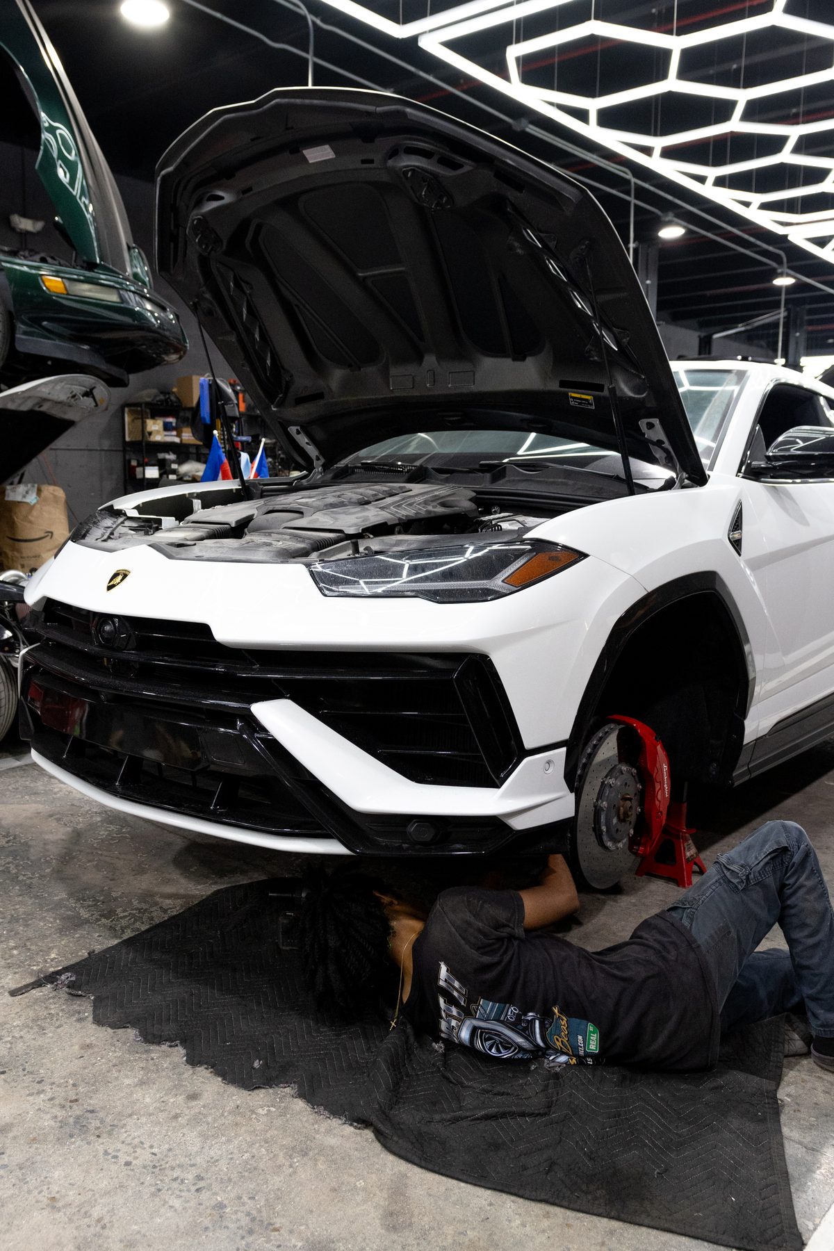 White Lamborghini Urus with hood up and a technician underneath